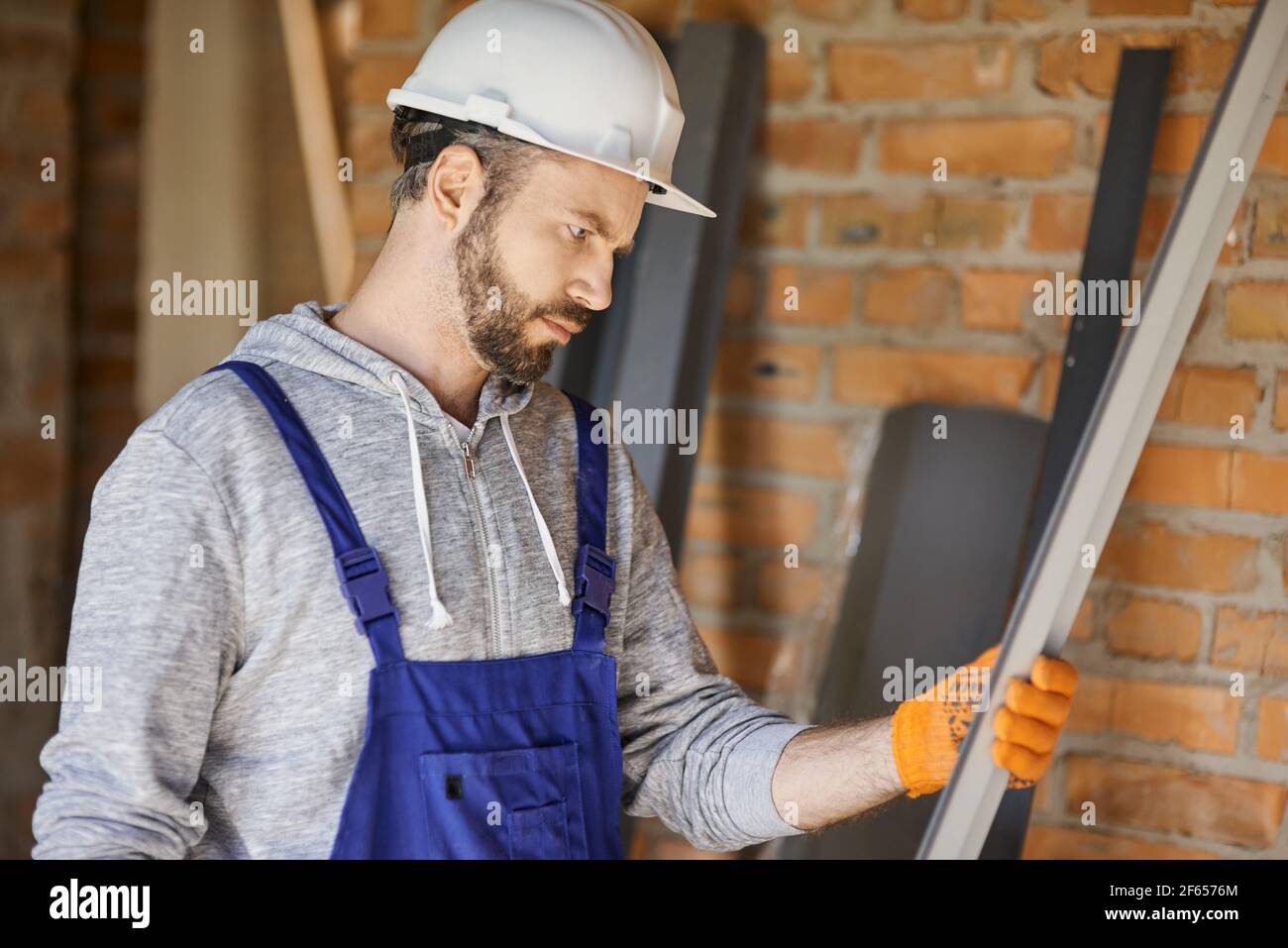 Portrait of focused male builder wearing overalls and hard hat holding a metal stud for drywall on interior site building Stock Photo