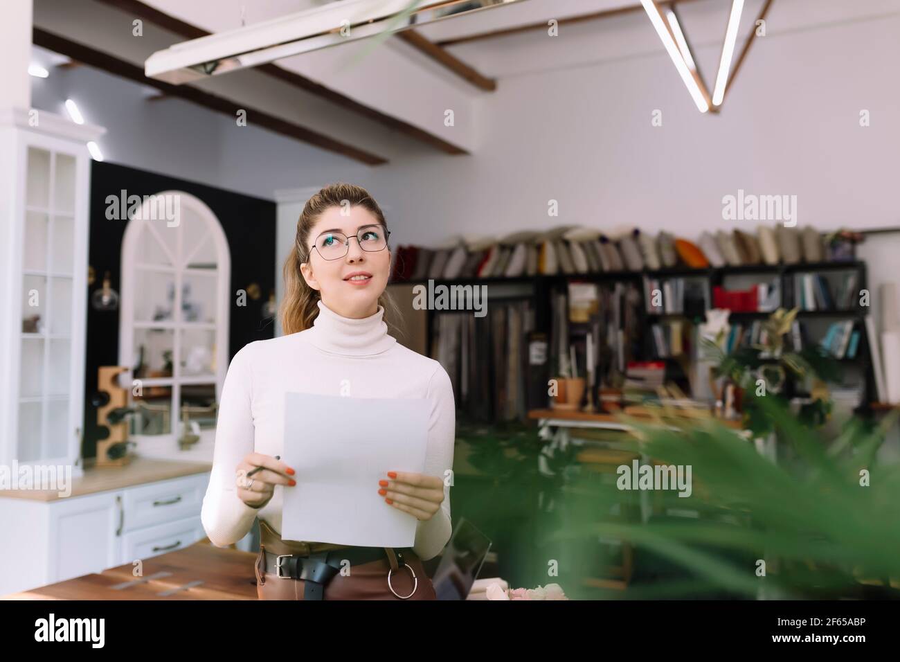 An interior designer is working on a new project, woman holding paper plan with pen. Considering the decision. Thinking about new design. High quality Stock Photo