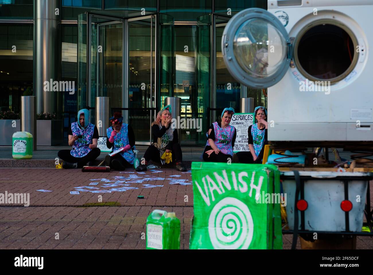 London, UK. 30th Mar, 2021. People dressed as old fashioned cleaners  demonstrate in front of Barclays Bank headquarters in Canary Wharf to bring  attention to the 'dirty money' that finances climate change