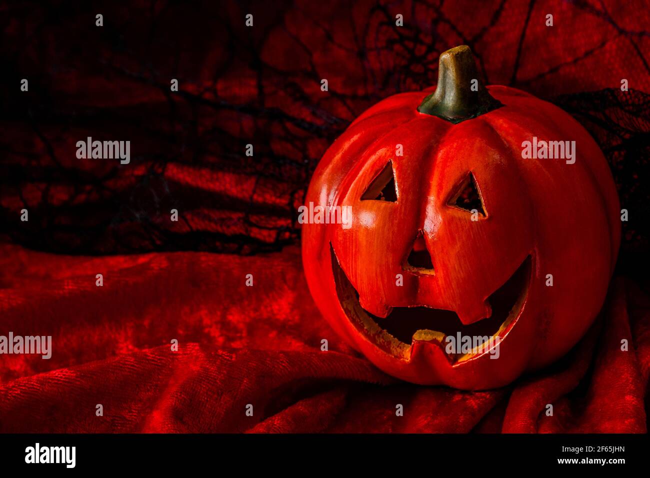 Halloween, trick or treat and fall holidays concept with a jack o'lantern pumpkin against a red, orange and spiderweb black lace background with copy Stock Photo