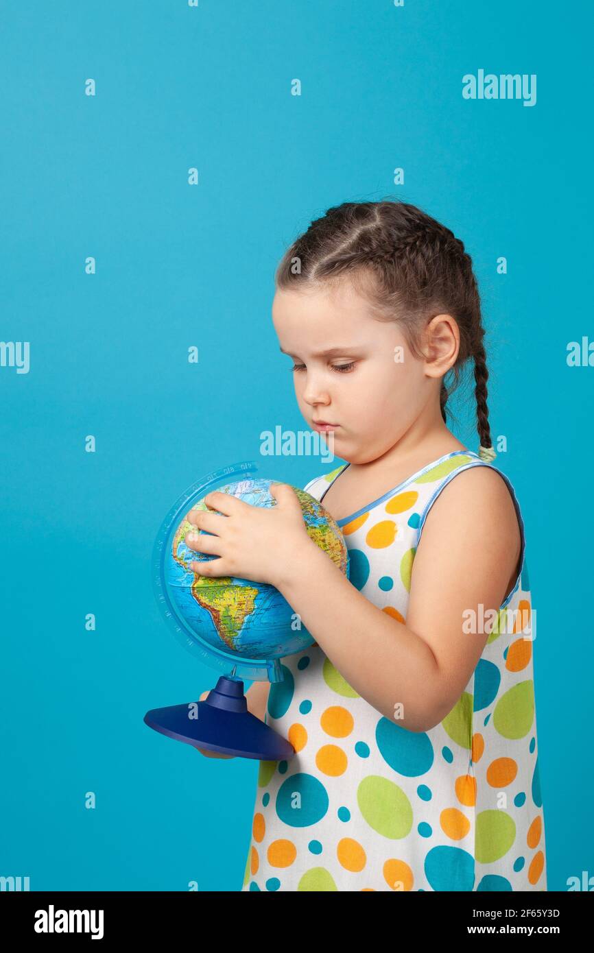 close-up portrait of distressed crying girl in white summer dress hugging globe and worrying about ecology of planet, isolated on a blue background Stock Photo
