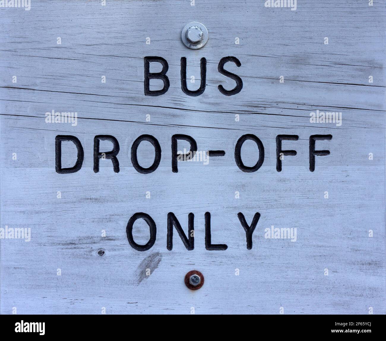 Close view of a bus drop off sign carved in wood with black lettering on gray paint. Stock Photo