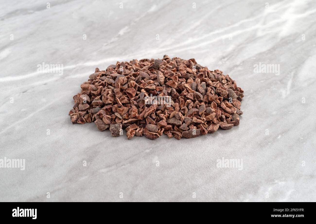 Side view of a portion of cocoa nibs on a gray marble countertop illuminated with natural light. Stock Photo