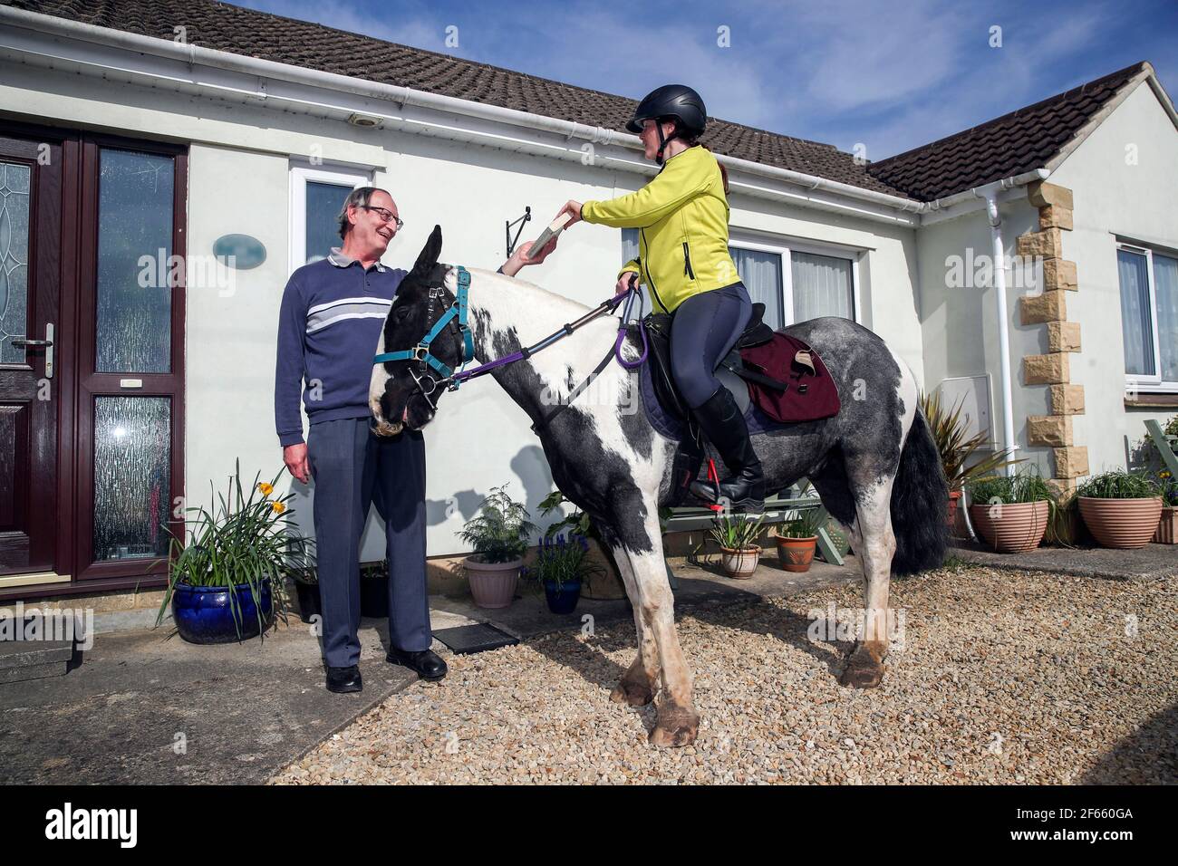 PLEASE NOTE: HOUSE PLAQUE HAS BEEN PIXELATED BY THE PA PICTURE DESK AT THE OWNERS REQUEST Rescue pony Micky helps owner Abi Eliot-Williams deliver library books to Mike Scott, a member of the Hullavington Book Group in the village of Hullavington near Malmesbry, Wiltshire. Micky was rescued as a colt after being found abandoned in poor conditions on a farm and taken in by the Blue Cross before being adopted by Abi. Picture date: Tuesday March 30, 2021. Stock Photo