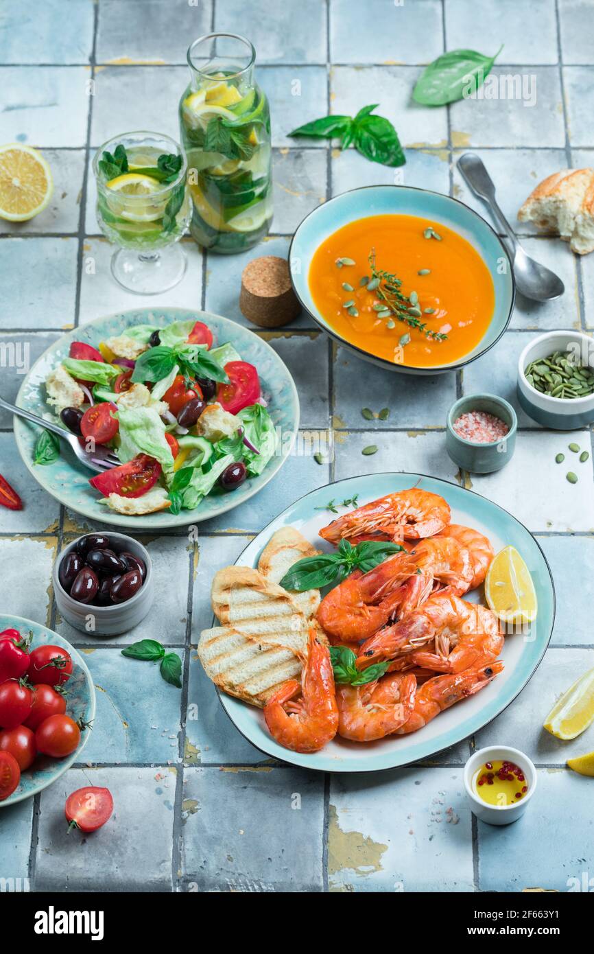 Mediterranean dishes at tiles table: seafood shrimps, vegetable salad, pumpkin soup, seeds and fruit lemonade Stock Photo