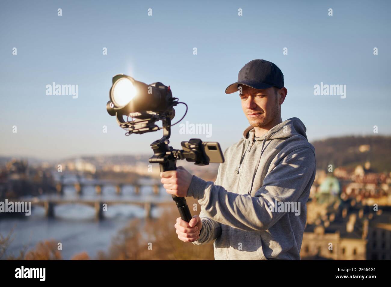 Young man filming with camera and gimbal. Filmmaker standing against urban skyline. Prague, Czech Republic Stock Photo