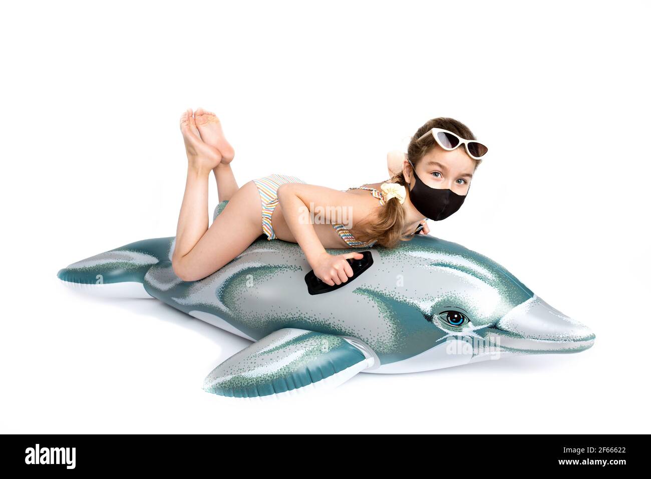 Child in a medical mask covid19 in a bathing suit on an inflatable dolphin. Studio photography on a white background.  Stock Photo