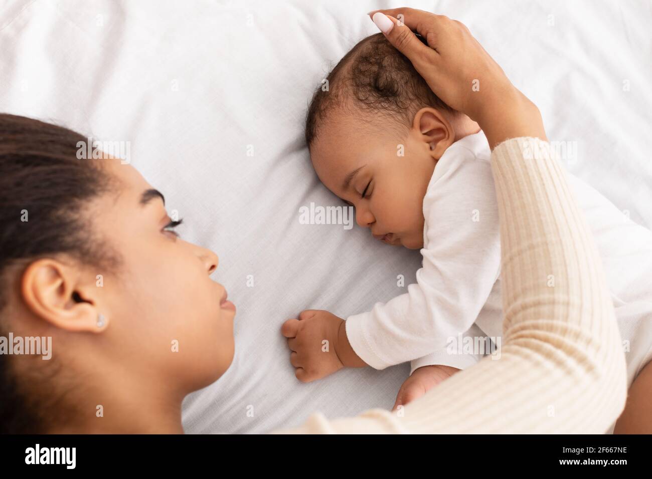 African Mom Stroking Sleeping Baby Lying In Bed Indoor Stock Photo
