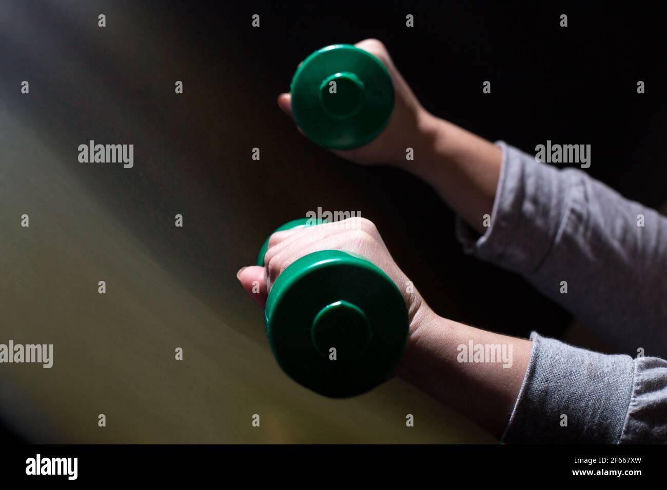 Woman's hands doing exercises with dumbbells on black background with copy space. Stock Photo