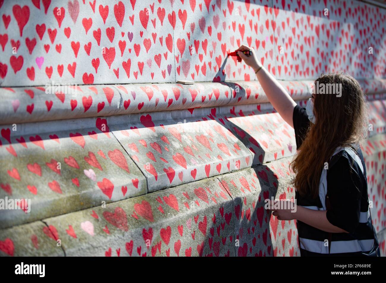 London, UK. 30th Mar, 2021. Hearts are drawn onto the Covid Memorial Wall on the South Bank, opposite the Houses of Parliament. The volunteers are drawing one heart for each of the 145,000 people who have died so far from the Coronavirus in the UK. Credit: Mark Thomas/Alamy Live News Stock Photo