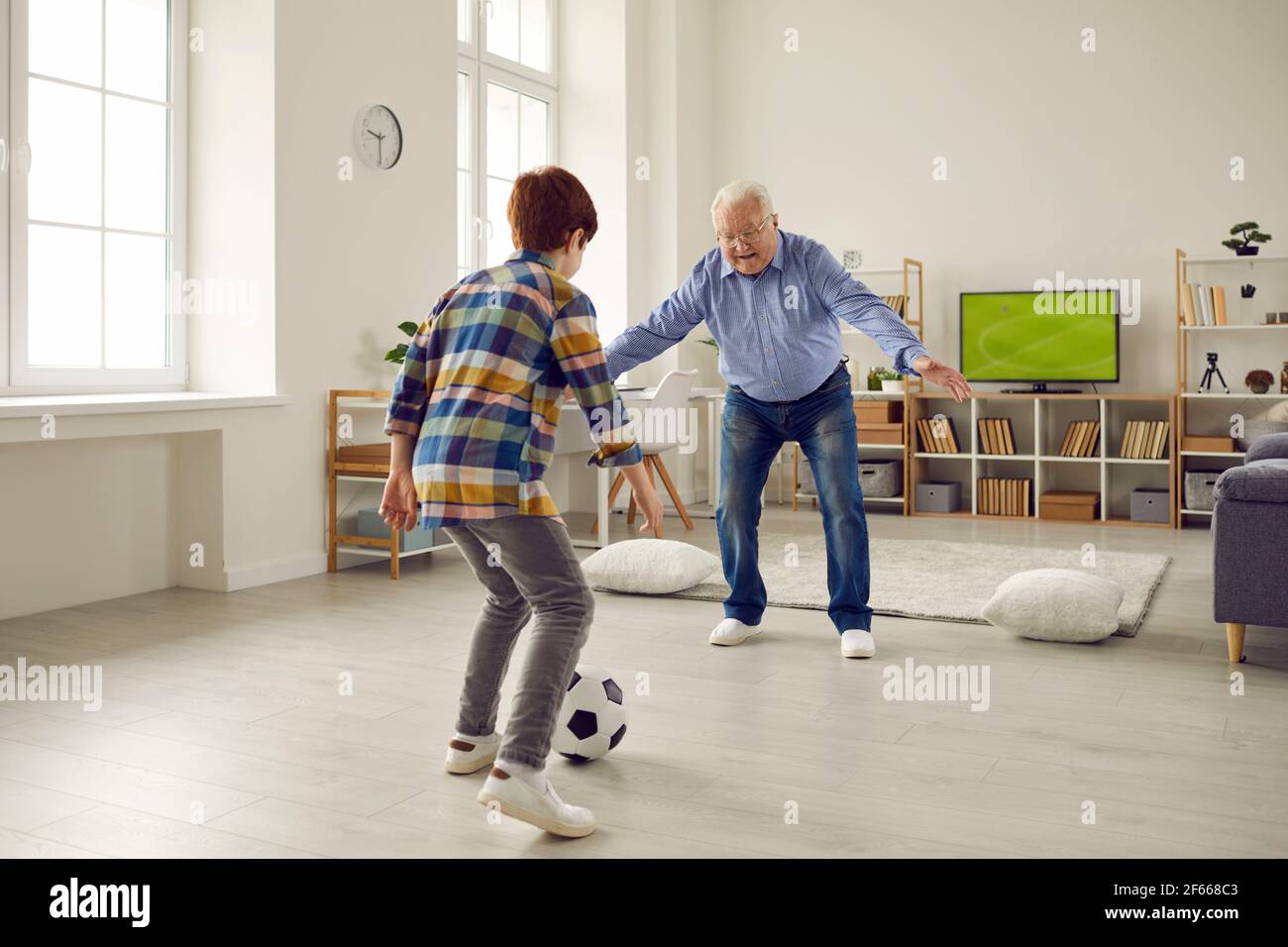 Elderly grandfather playing football with grandson in home living room Stock Photo