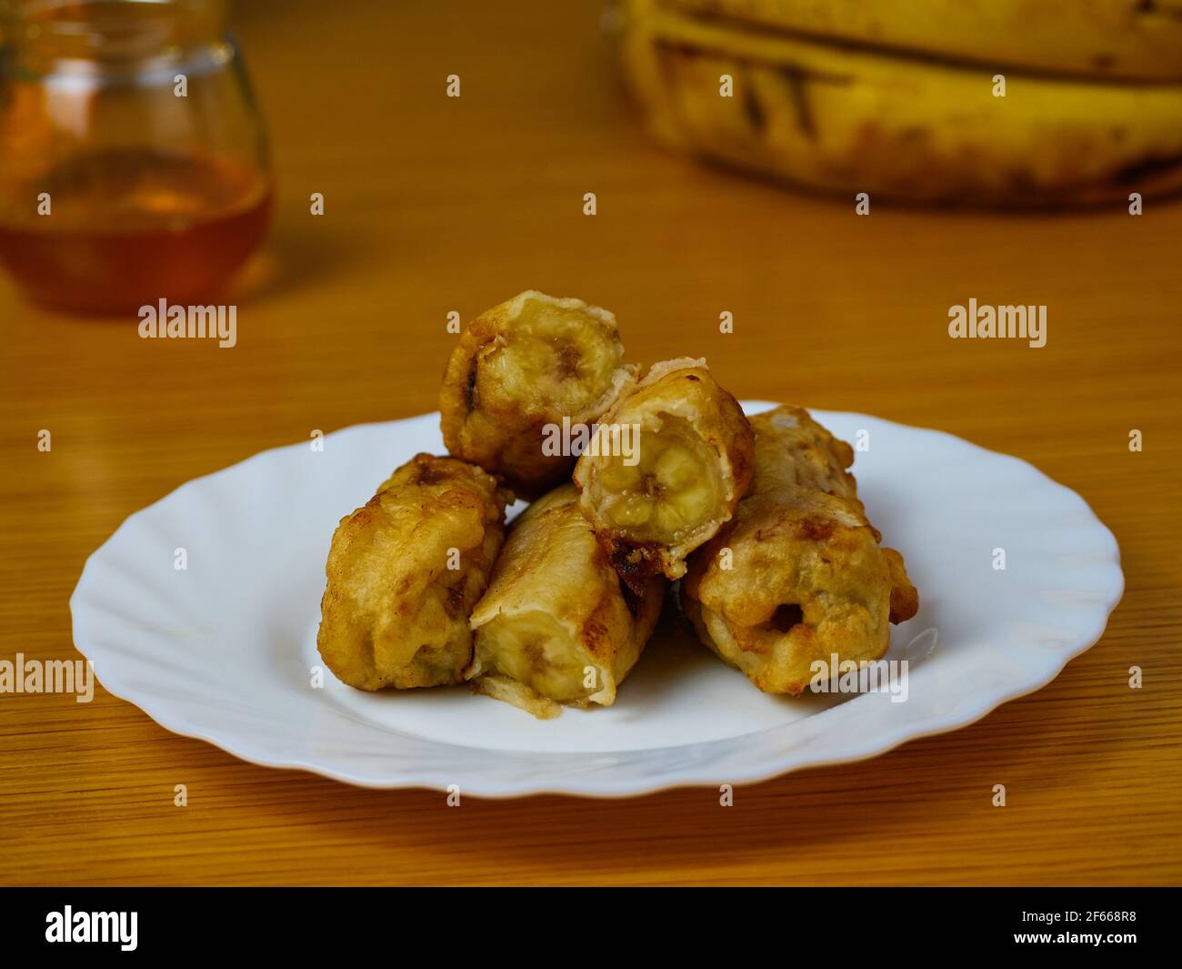 Fried slices of the ripe plantain on a white dish decorated with bananas and honey Stock Photo