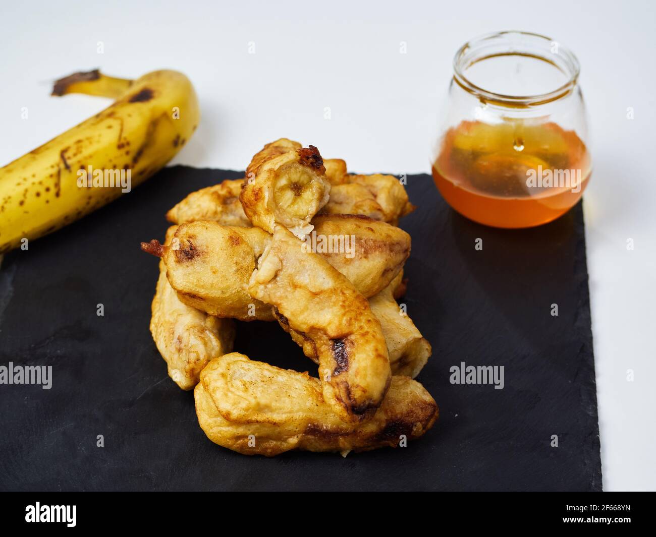 Fried slices of the ripe plantain decorated with a banana and honey on a black slate board Stock Photo