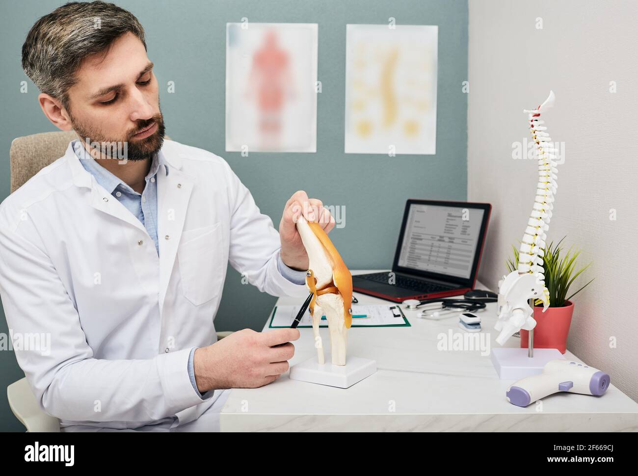 Mature doctor using a knee-joint anatomical model to analyze human knee problem areas and treatment Stock Photo