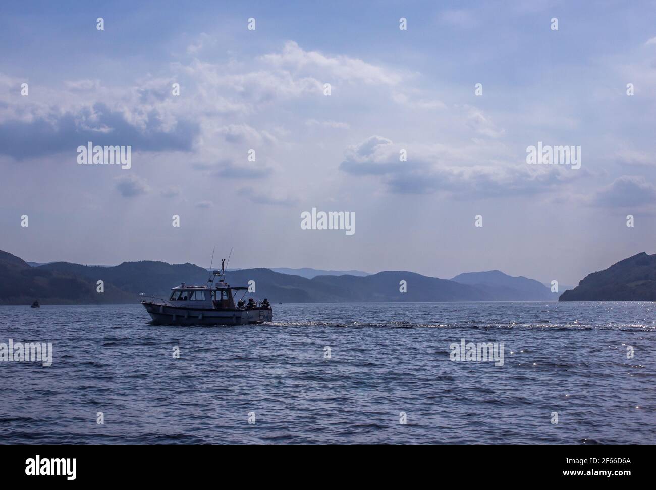 A tourist boat on the vast blue surface of Loch Ness, Scotland with the mountains which form the edge of the great Glen in the distance Stock Photo