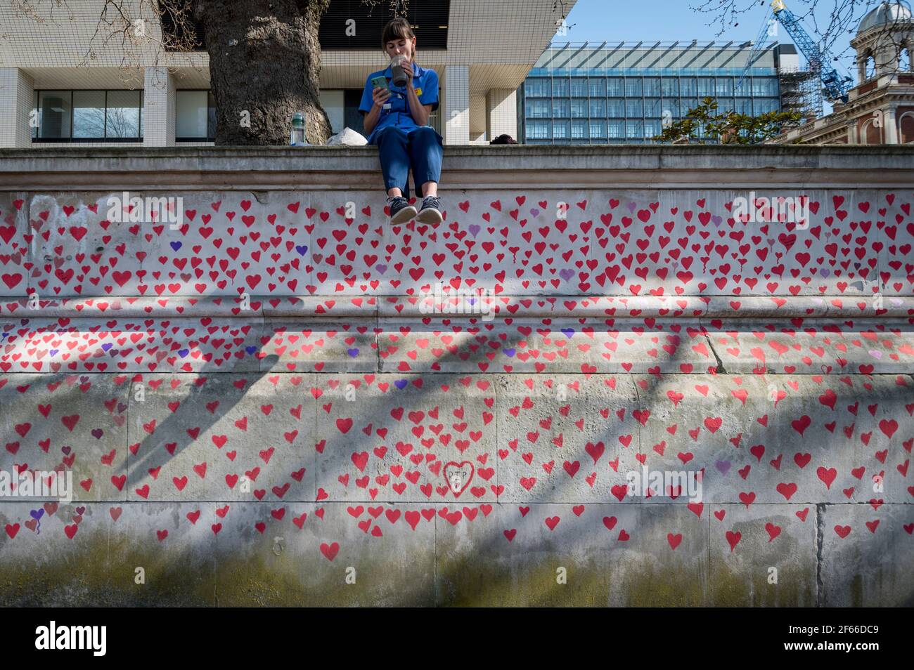London, UK. 30th Mar, 2021. An NHS worker above hearts on a wall in Lambeth by the River Thames, with each heart representing someone who died during the UK's ongoing coronavirus pandemic. Called The National Covid Memorial Wall, it has been created by the Covid-19 Bereaved Families for Justice and will extend for half a mile by the time it is complete. Credit: Stephen Chung/Alamy Live News Stock Photo