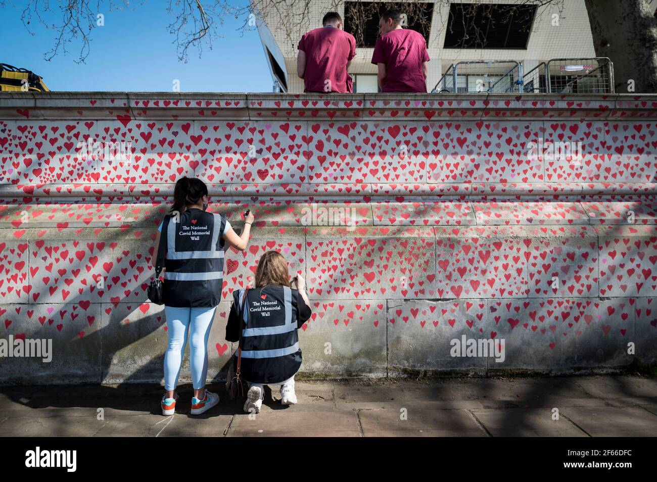 London, UK. 30th Mar, 2021. NHS workers above volunteers drawing hearts on a wall in Lambeth by the River Thames, with each heart representing someone who died during the UK's ongoing coronavirus pandemic. Called The National Covid Memorial Wall, it has been created by the Covid-19 Bereaved Families for Justice and will extend for half a mile by the time it is complete. Credit: Stephen Chung/Alamy Live News Stock Photo