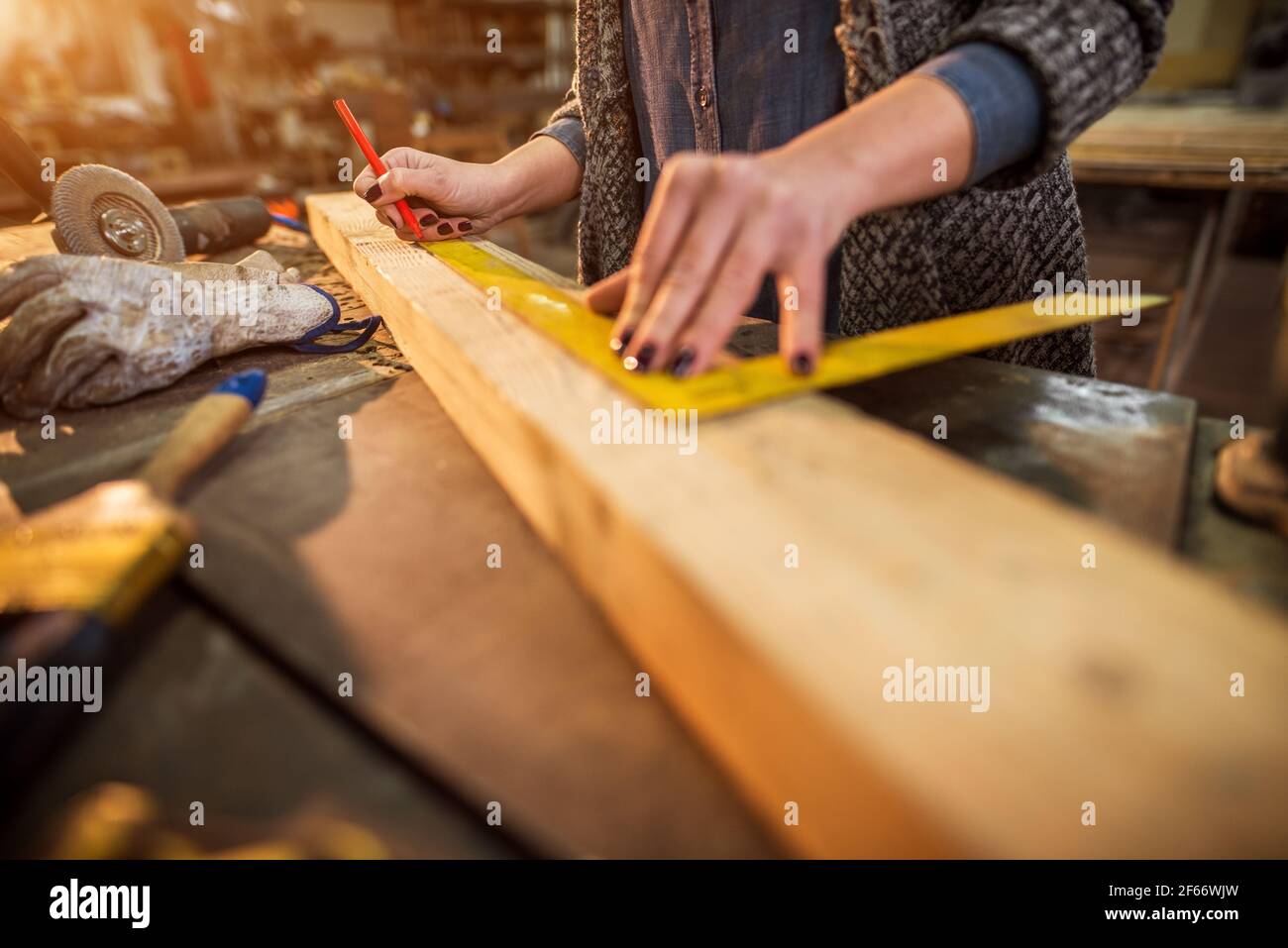 Close up view of hardworking professional carpenter woman hands working with a ruler and making marks on the wood at the table in the fabric workshop. Stock Photo