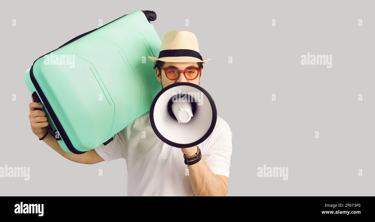 Man tourist talking in megaphone holding travel suitcase on shoulder portrait Stock Photo