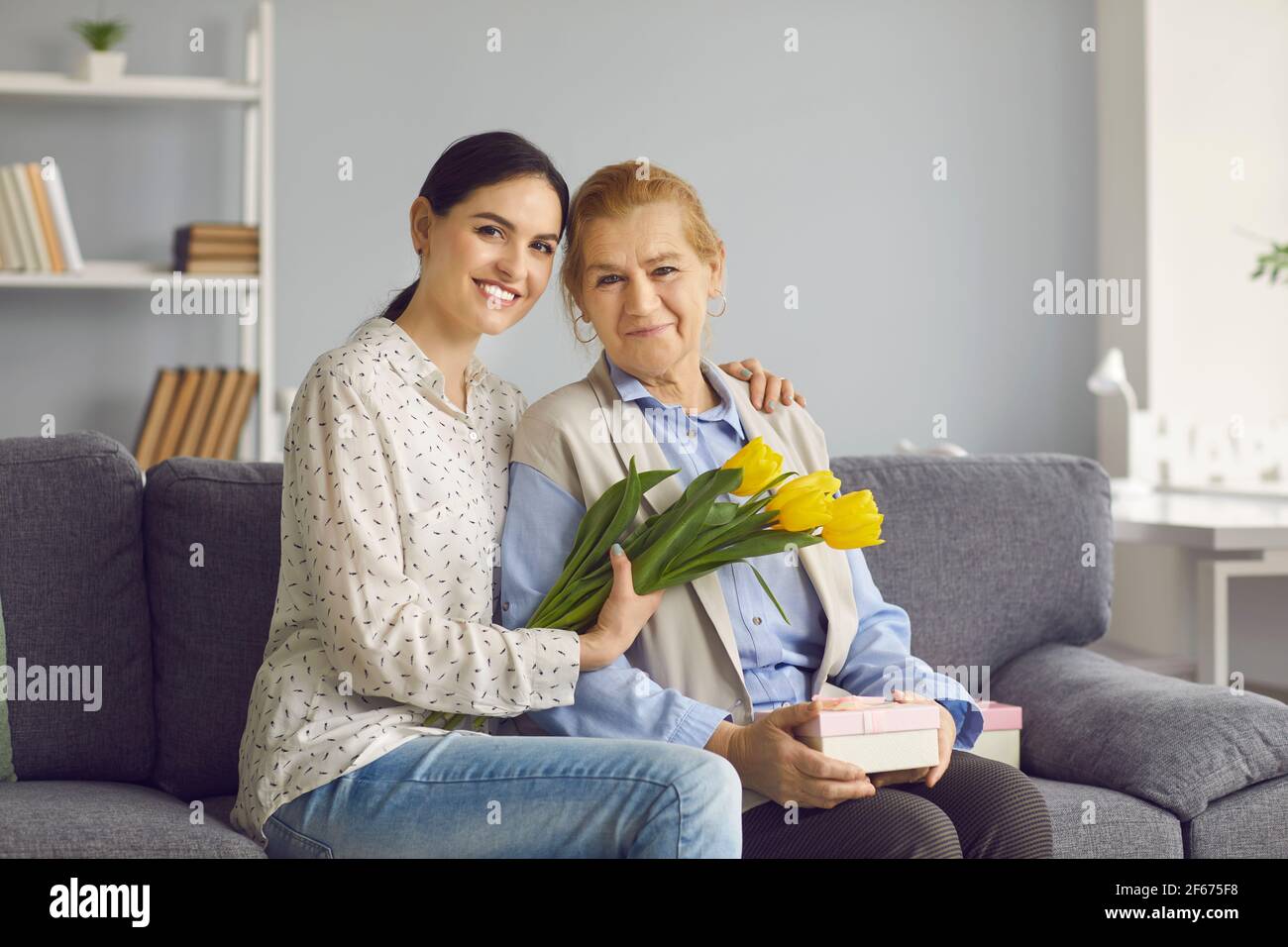 Portrait of young grownup daughter with flower embracing elderly mother Stock Photo