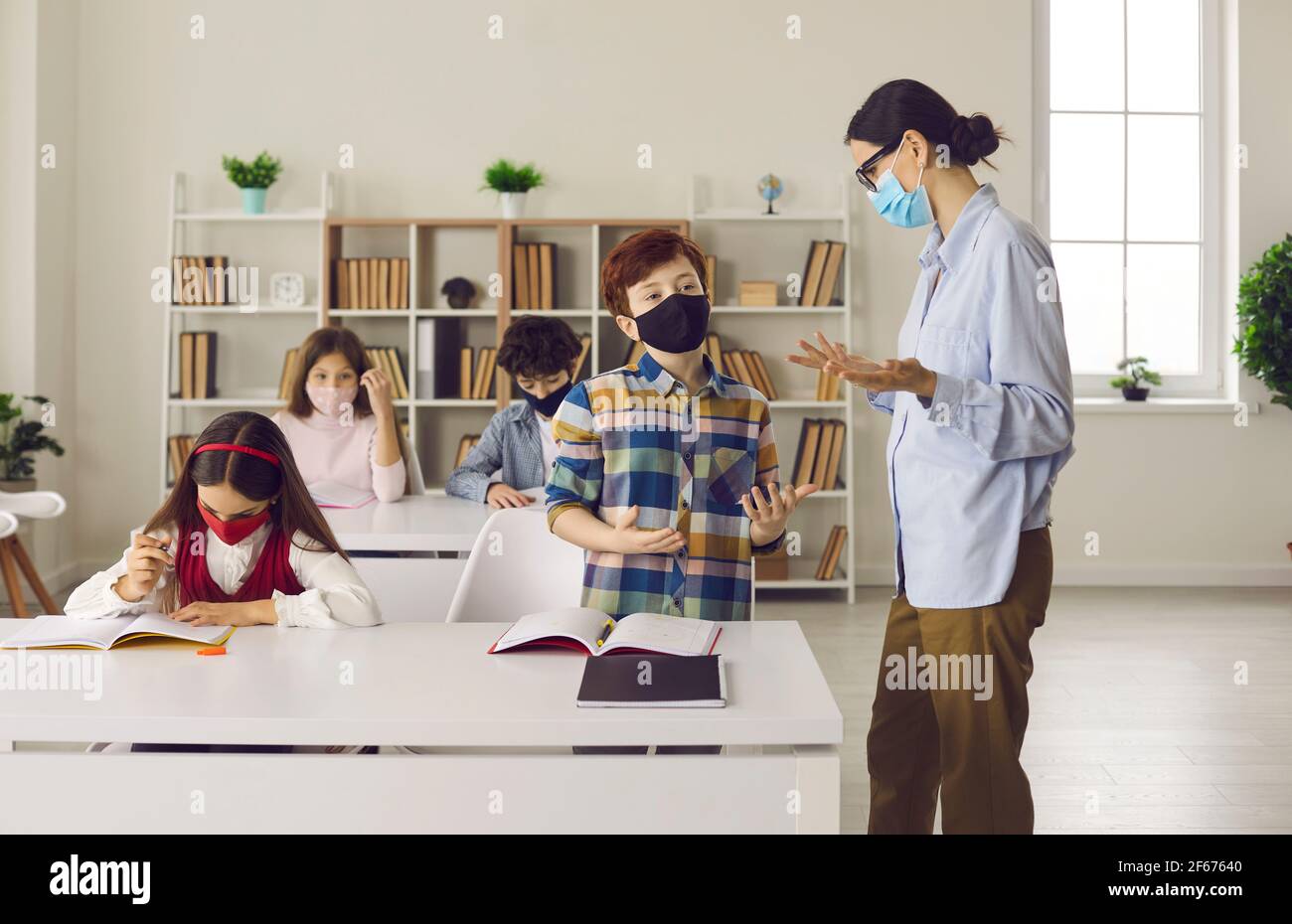 Elementary school student in medical face mask answering teacher's question in class Stock Photo