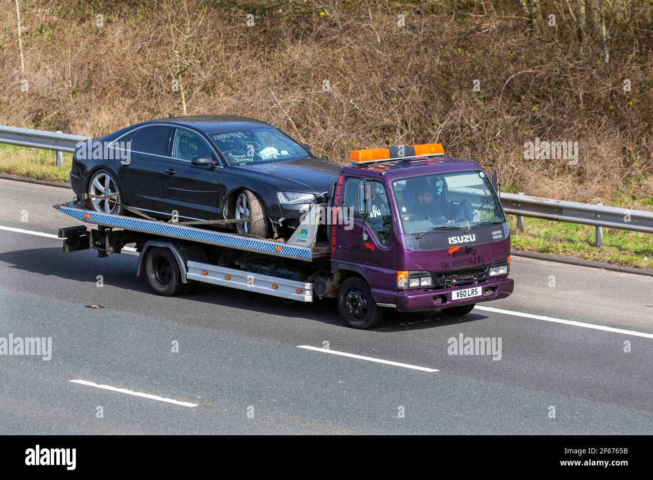 1999 90s nineties Isuzu Npr 65 P 3856cc diesel HCV towing damaged car with deployed airbag & bonnet jammed; Road accident car recovery trailer; 24 hr breakdown commercial breakdown service; Travelling on the M61 motorway, UK Stock Photo
