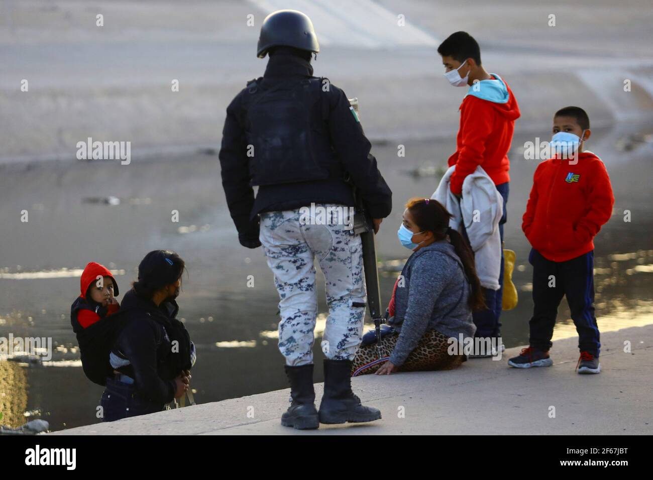 A member of the Guardia Nacional  (National Guard) speaks with a family of migrants before crossing the Rio Bravo river to turn themselves into U.S Border Patrol agents to request asylum in El Paso, Texas, U.S., as seen from Ciudad Juarez, Mexico, March 30, 2021. REUTERS/Edgard Garrido Stock Photo