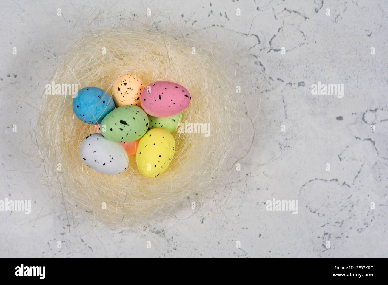 Multicolored Easter eggs in a nest on a white concrete background. Stock Photo