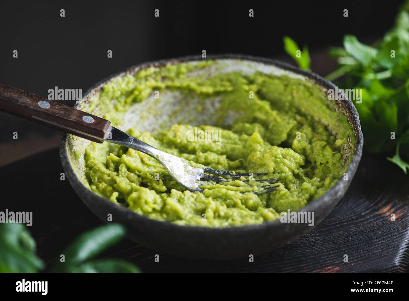 Mashed avocado sauce in a bowl on dark background. Healthy vegan avocado sauce Stock Photo
