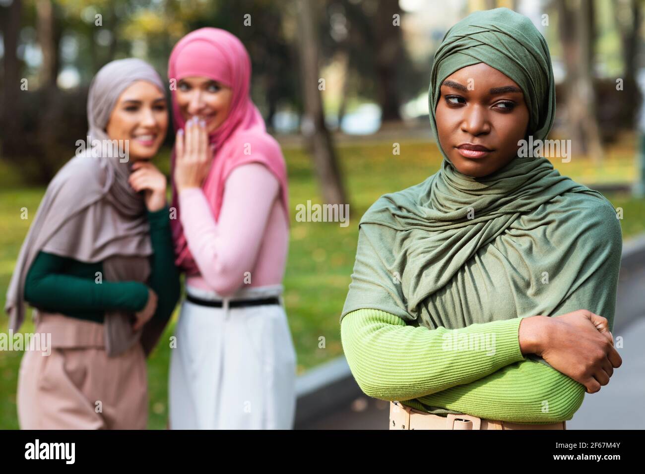 Arabic Ladies Whispering Behind Back Of Black Muslim Woman Outdoors Stock Photo