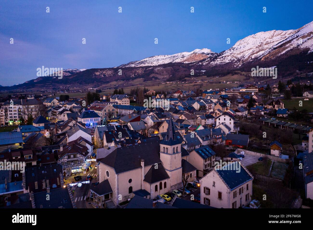 Evening drone view on mountain village in Vercors mountains, France. Snow layer covering mountain ridge in background. Stock Photo