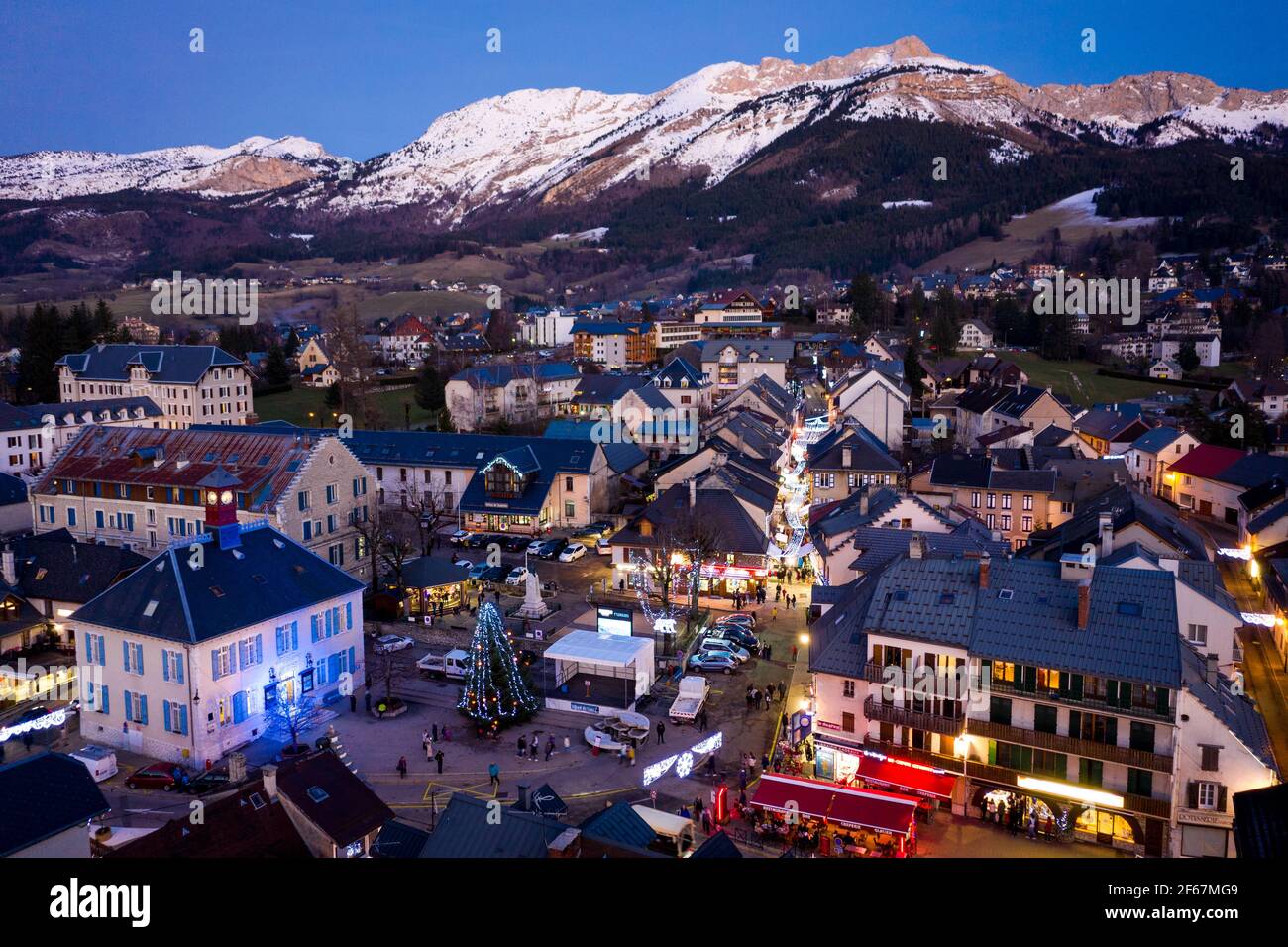 Aerial evening view of houses in mountain village. Blue hour photo with snowcapped mountains in background, Vercors, France. Stock Photo