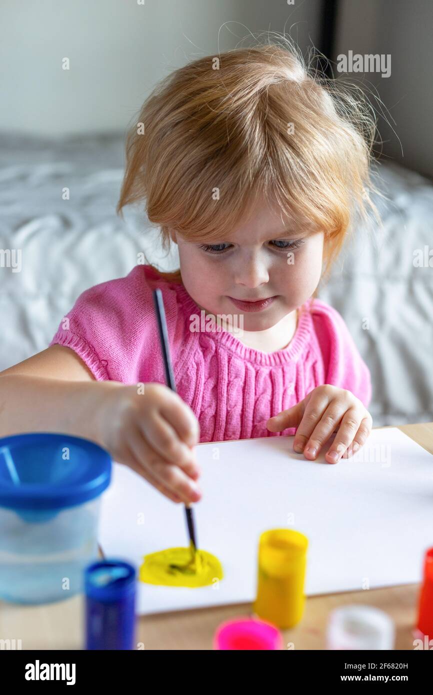 Little smiling girl painting on paper with colorful paints sitting at the table at home Stock Photo