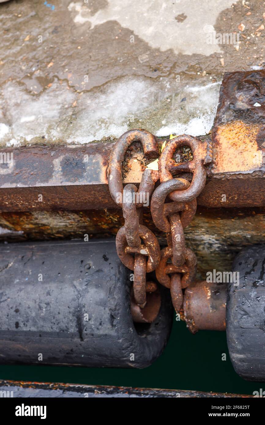 An old rusty chain connecting the rubber pipe bumpers on the sea pier. A fragment of the pier. Stock Photo