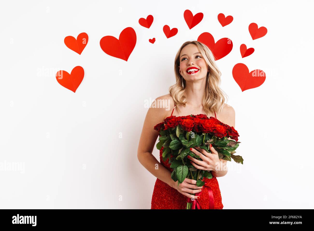 Happy beautiful girl in red dress smiling and holding roses isolated ...