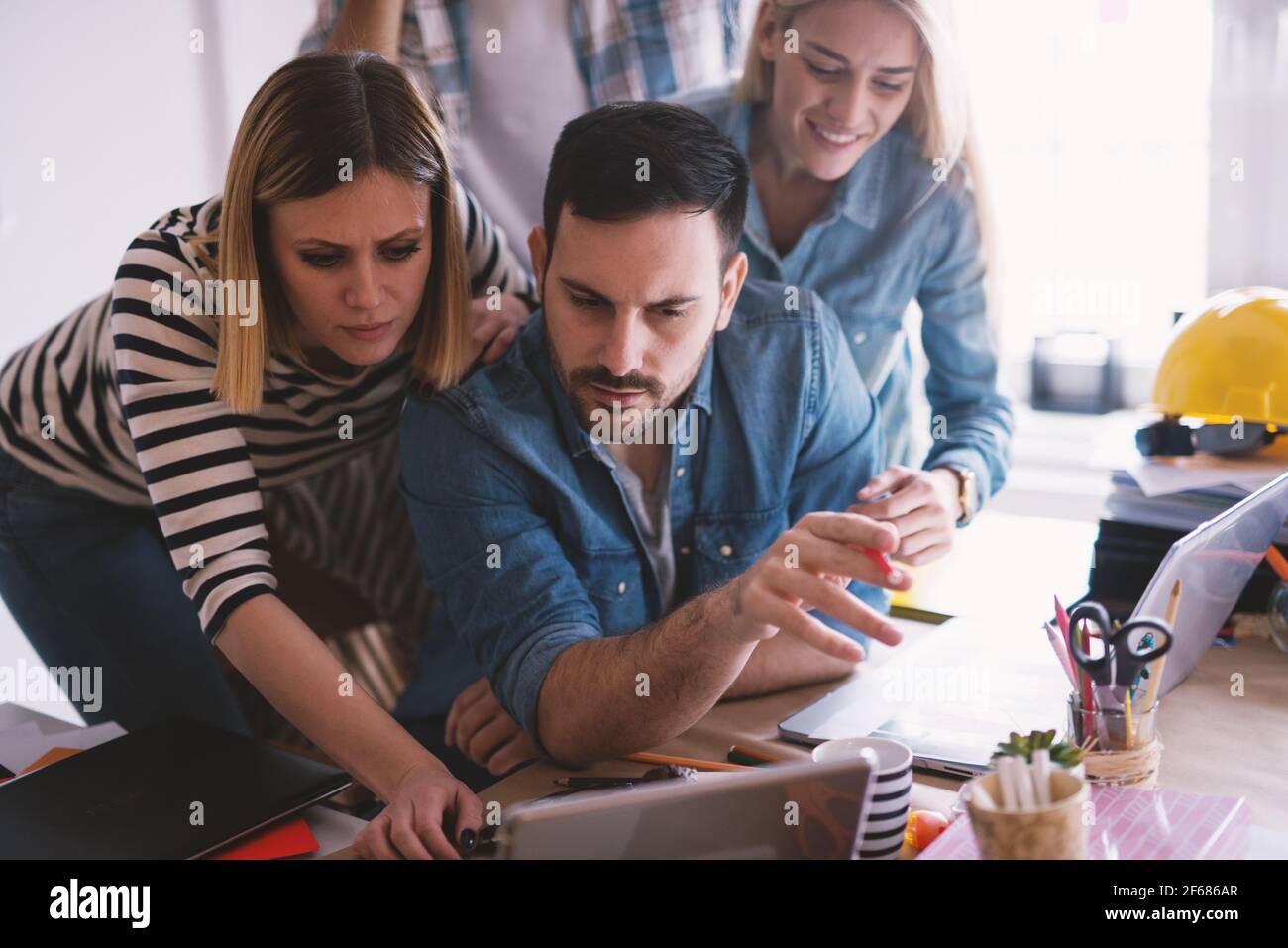 Group of curious smiling coworkers standing around their boss and watching project on a tablet. Stock Photo