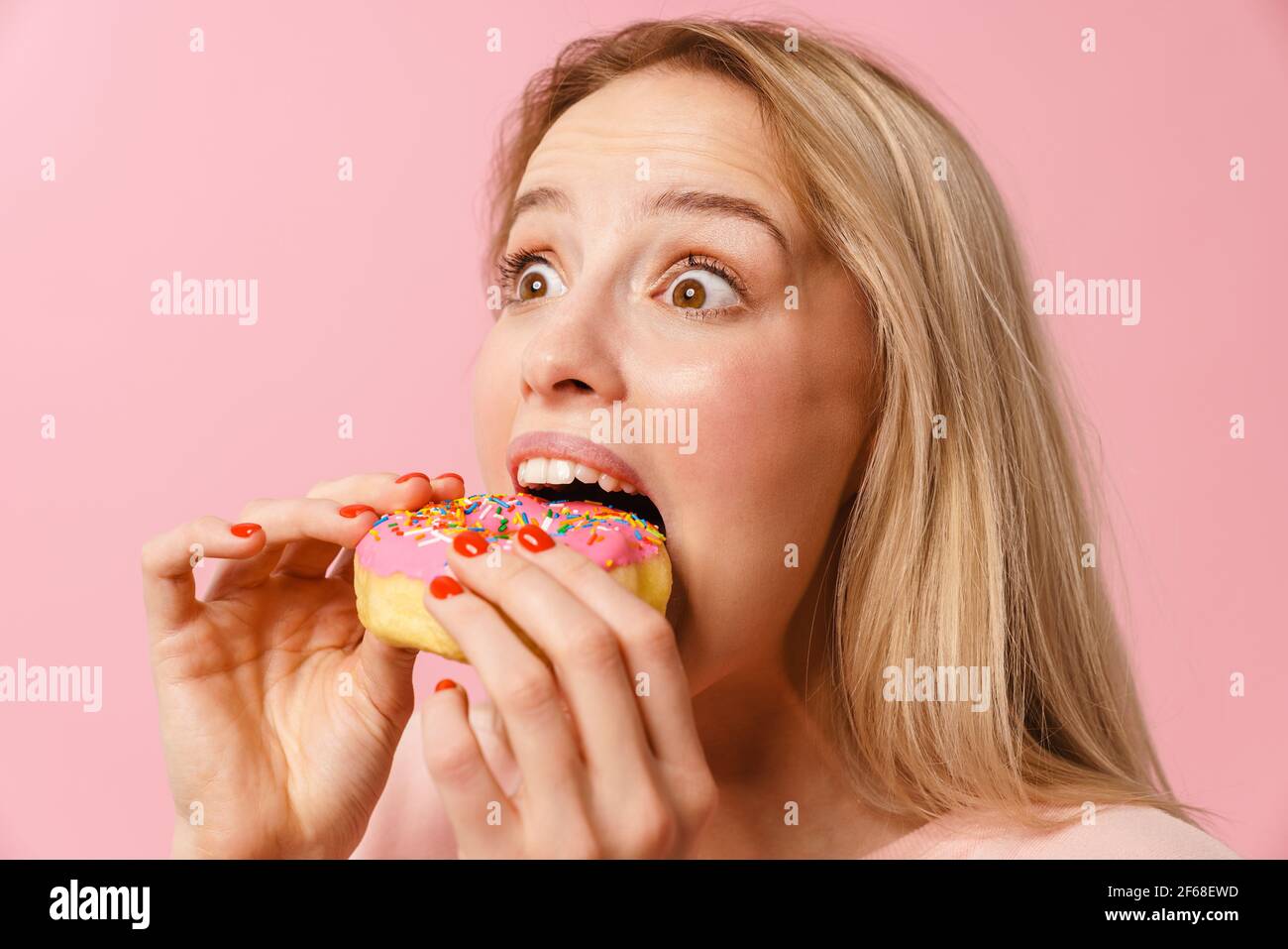 Shocked charming hungry girl eating doughnut on camera isolated over