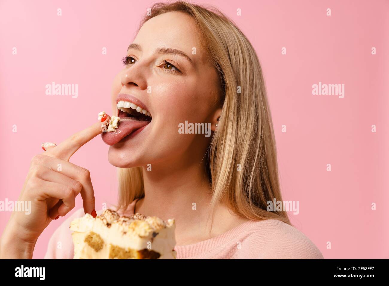 Joyful charming girl eating cake with her fingers isolated over pink