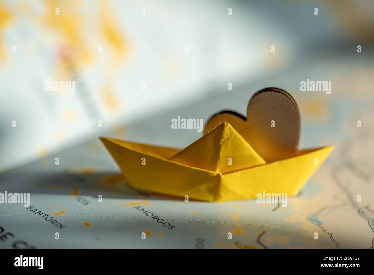 isolated origami yellow boat with wooden heart on world map. travel, sail or cruise concept, shipping or transportation through the sea. Stock Photo