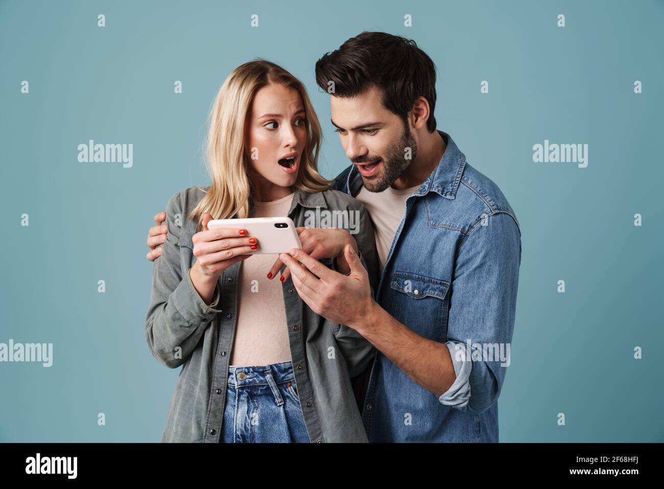 Young surprised man and woman hugging and using mobile phone isolated ...