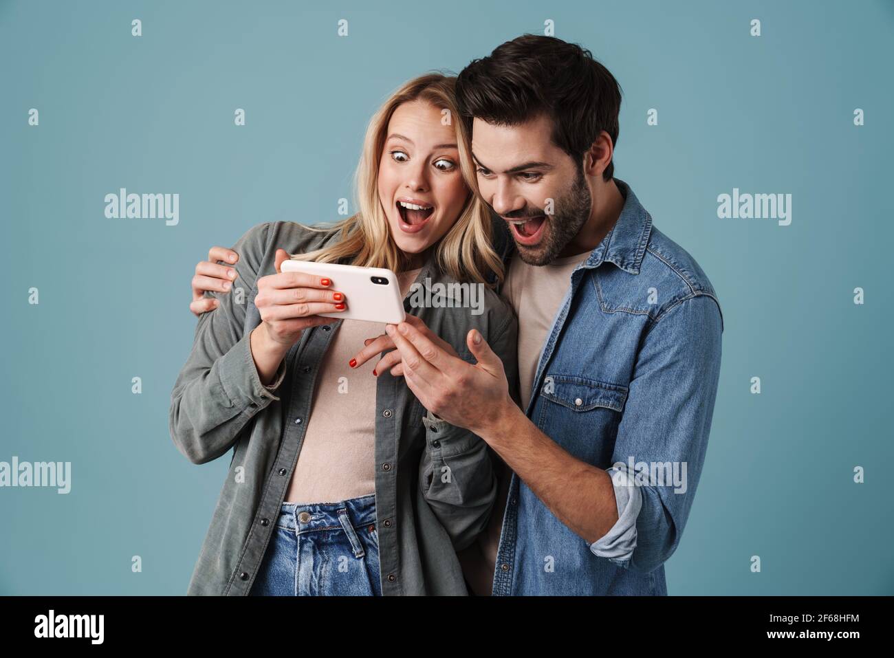 Young surprised man and woman hugging and using mobile phone isolated ...