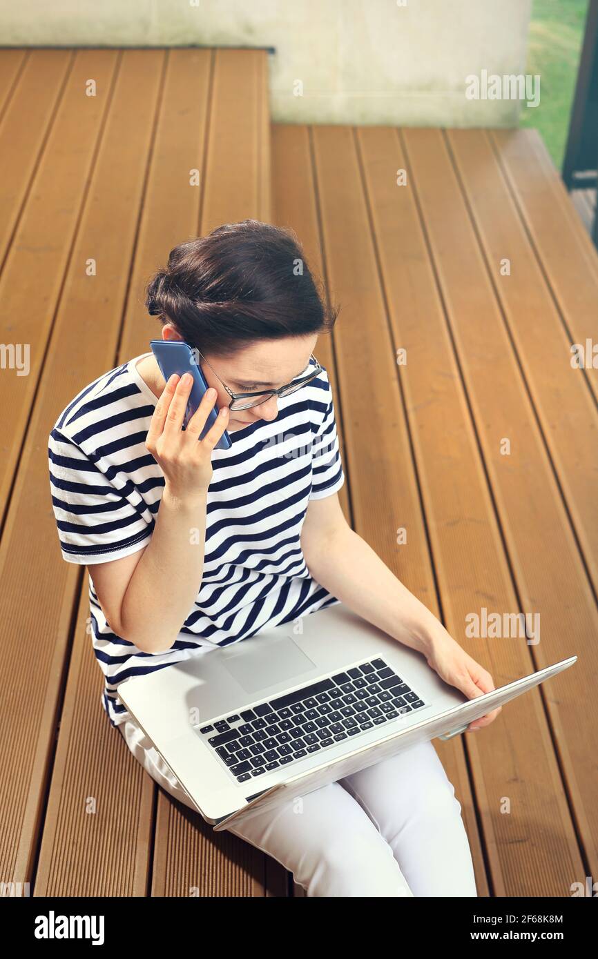 Home office work on a computer.  Work at home. Business woman working on the computer while sitting on the terrace of the house. Talking on the phone Stock Photo