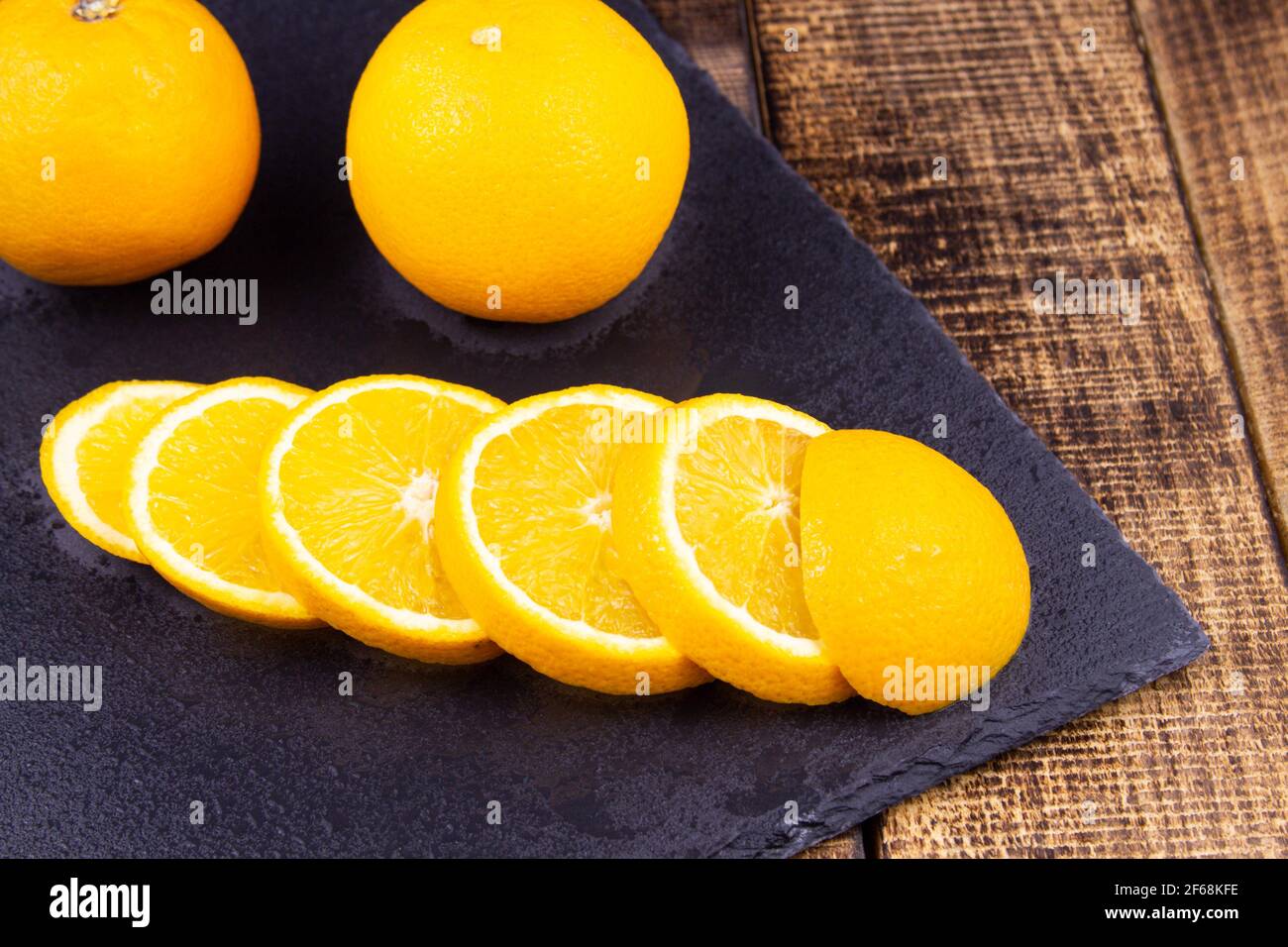 whole fruits and orange slices on a black tray on a wooden background. Stock Photo