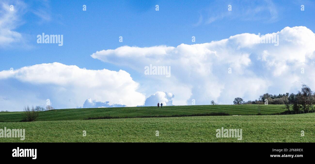 Two people walking down undulating fields near Piddington, Oxfordshire. Spring. Culmulus ciouds Stock Photo