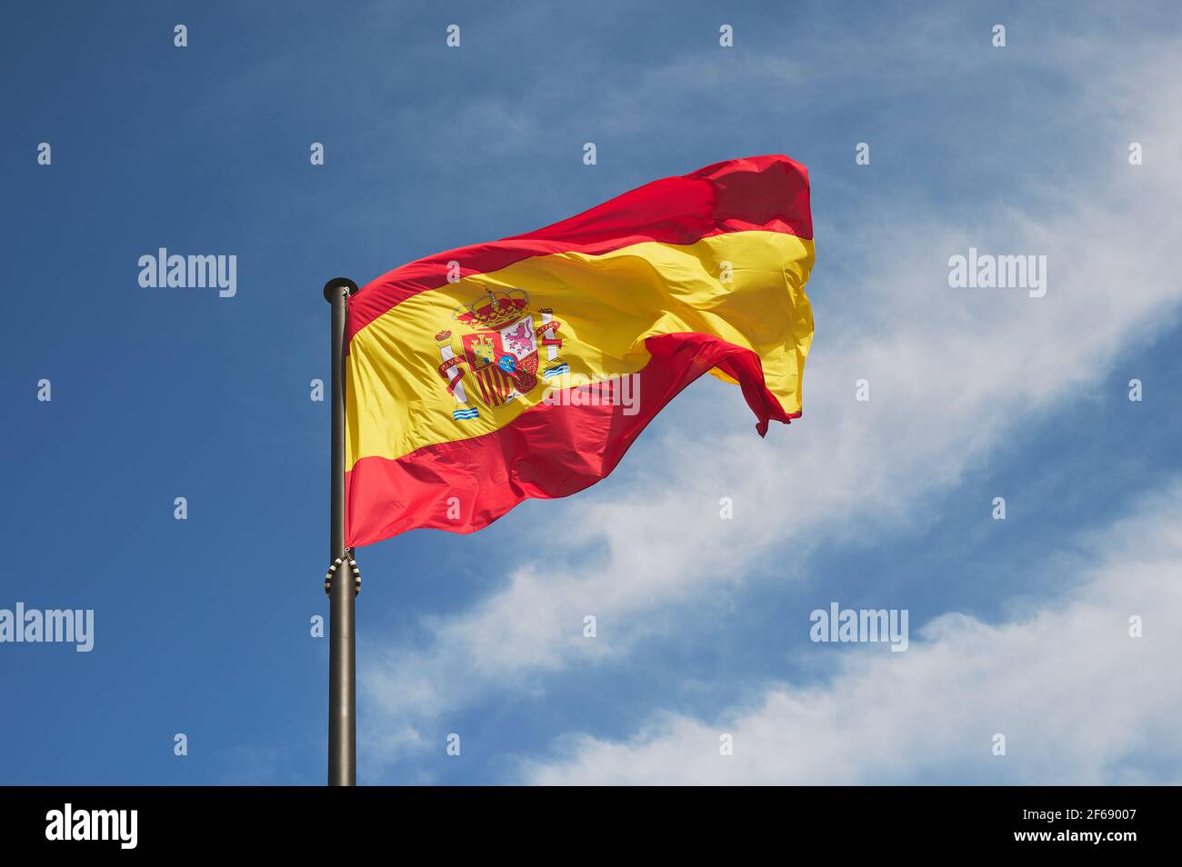 detail of the Spanish flag flying on a large black mast against a blue sky. Stock Photo