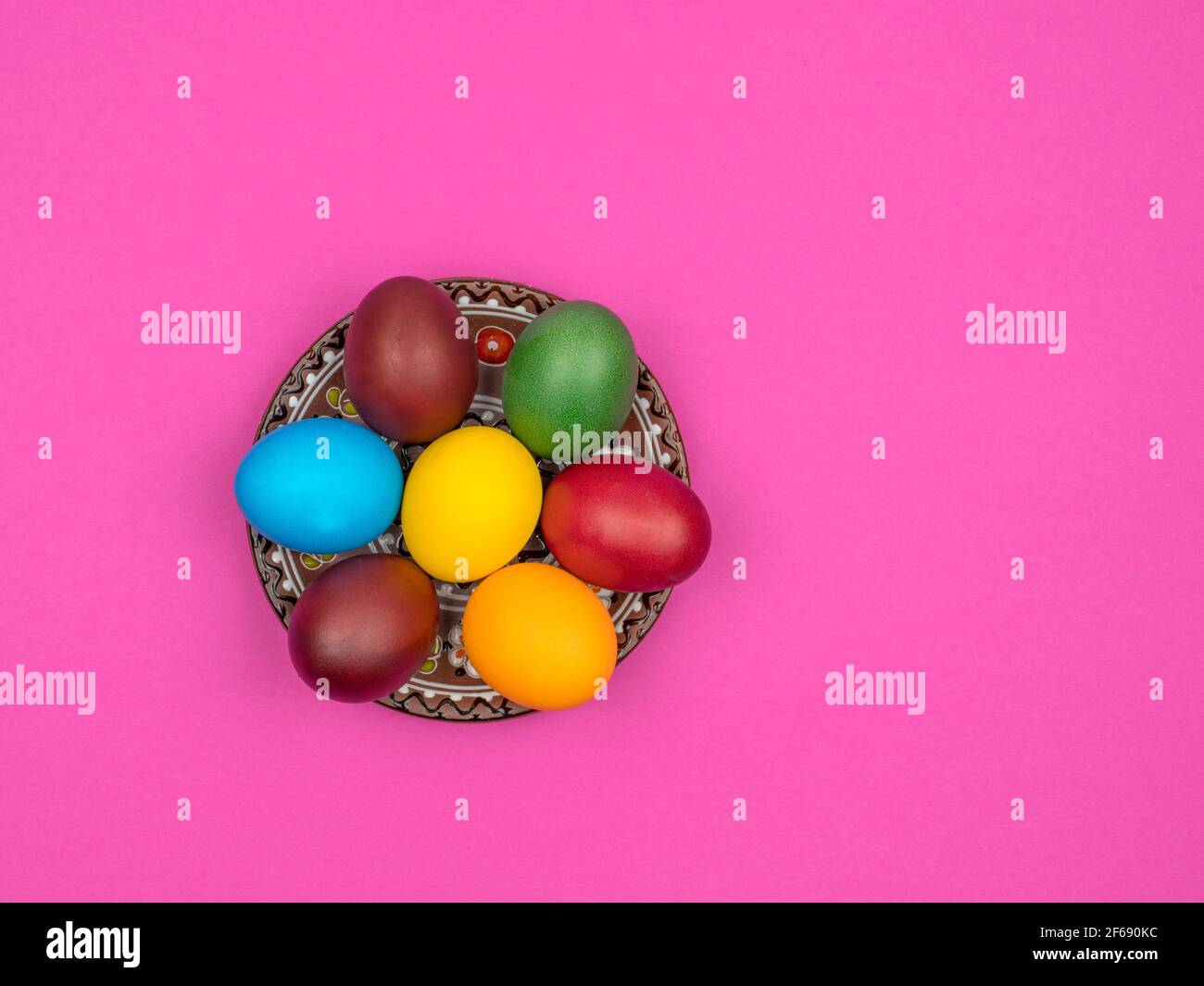 Bright colored eggs at Easter lie in a plate. Pink background. Stock Photo