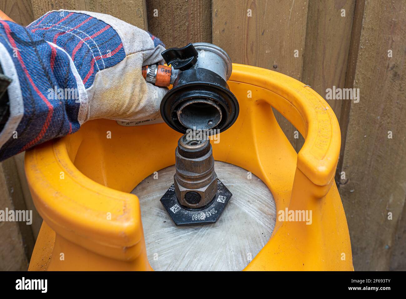 a hand with a glove mounts a Low Pressure Gas Regulator with Hose on a gas cylinder, Denmark, Mars 30, 2021 Stock Photo