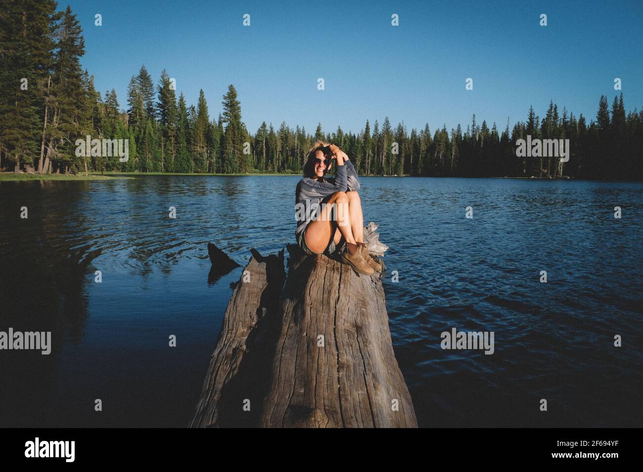 Blonde Woman Poses on a log over water at Sunset. Stock Photo