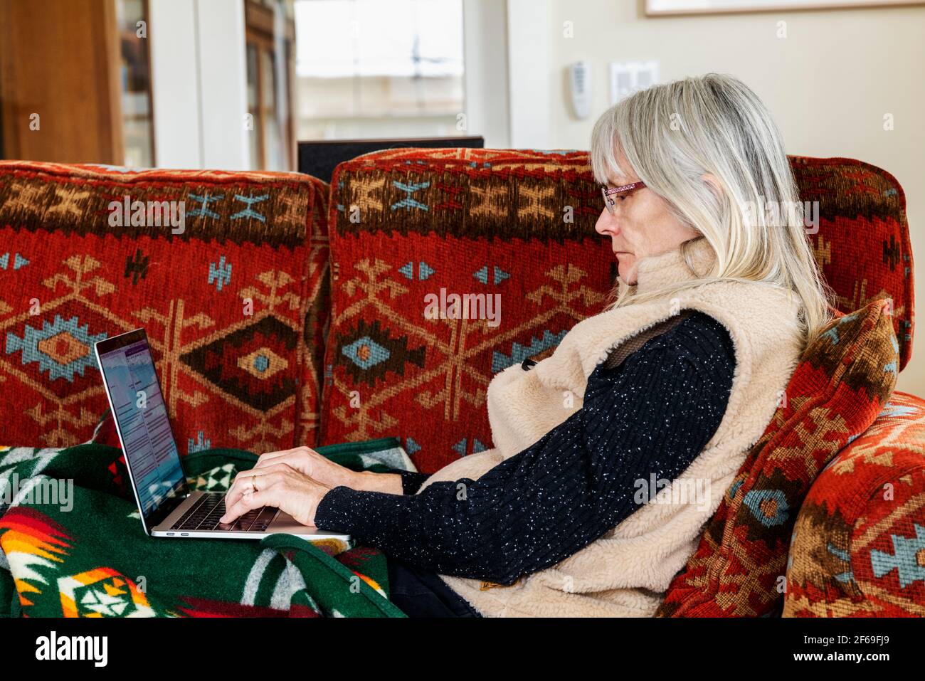 Senior woman seated on living room couch working on laptop computer Stock Photo