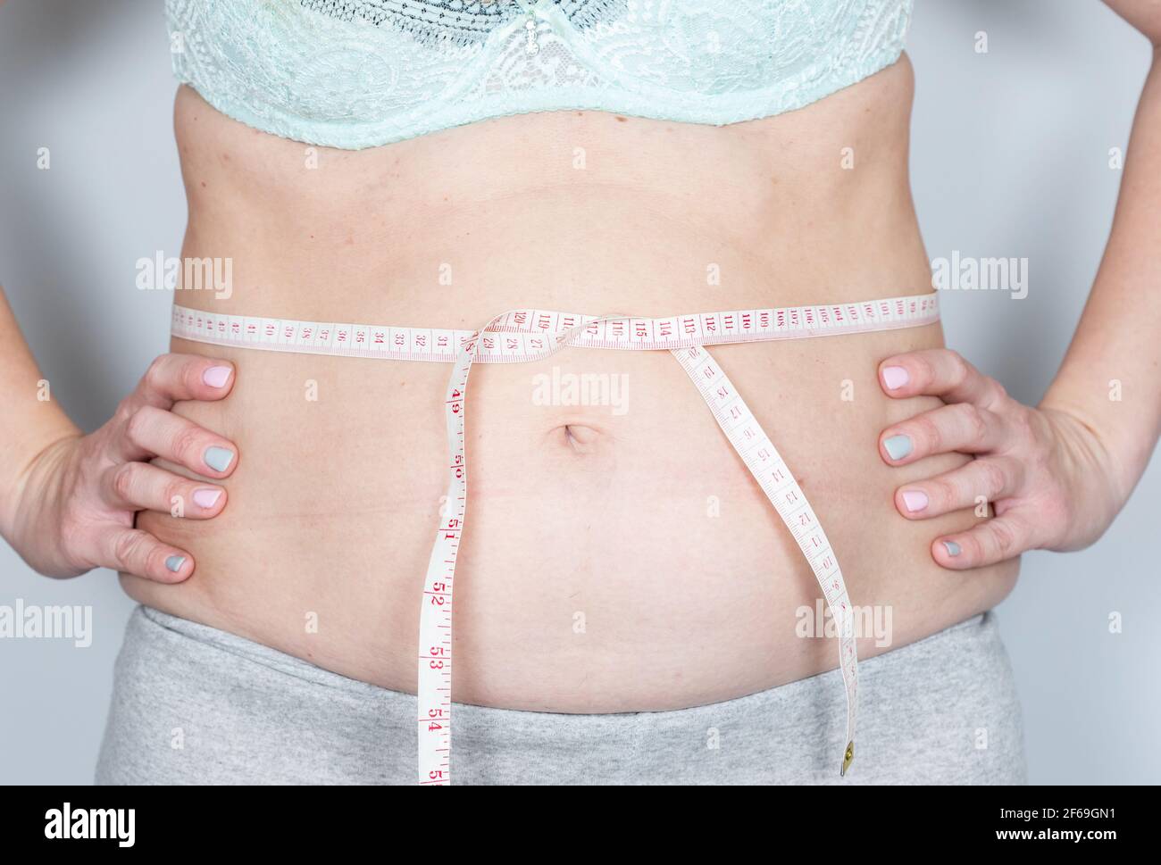 Overweight or fat adult woman is measureing around the body on the midriff on a gray background. Healthcare, medicine concept. Stock Photo